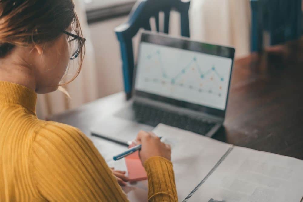 Businesswoman in yellow sweater analyzing data and graphs on her laptop for website management and digital marketing strategies.