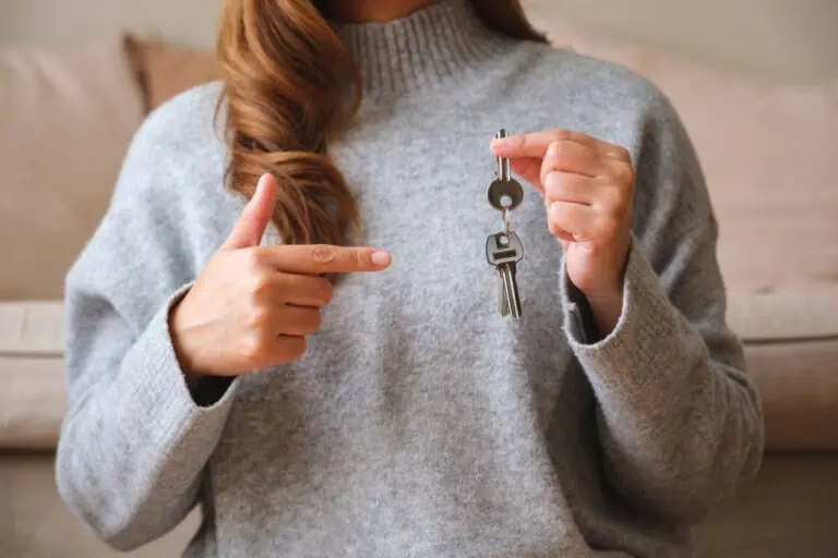 A woman in a gray sweater holding keys, symbolizing business ownership and asset control, in a professional setting.